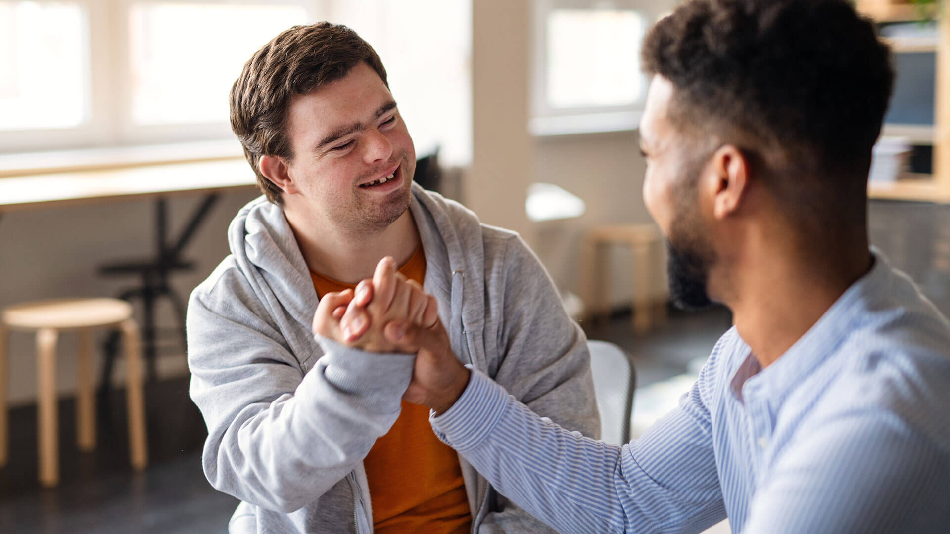 The Plus Sides of Becoming a NDIS Provider: A Disability Support Worker Shakes Hands With a Man With Downs Syndrome. The Two Men Are Smiling at Each Other.