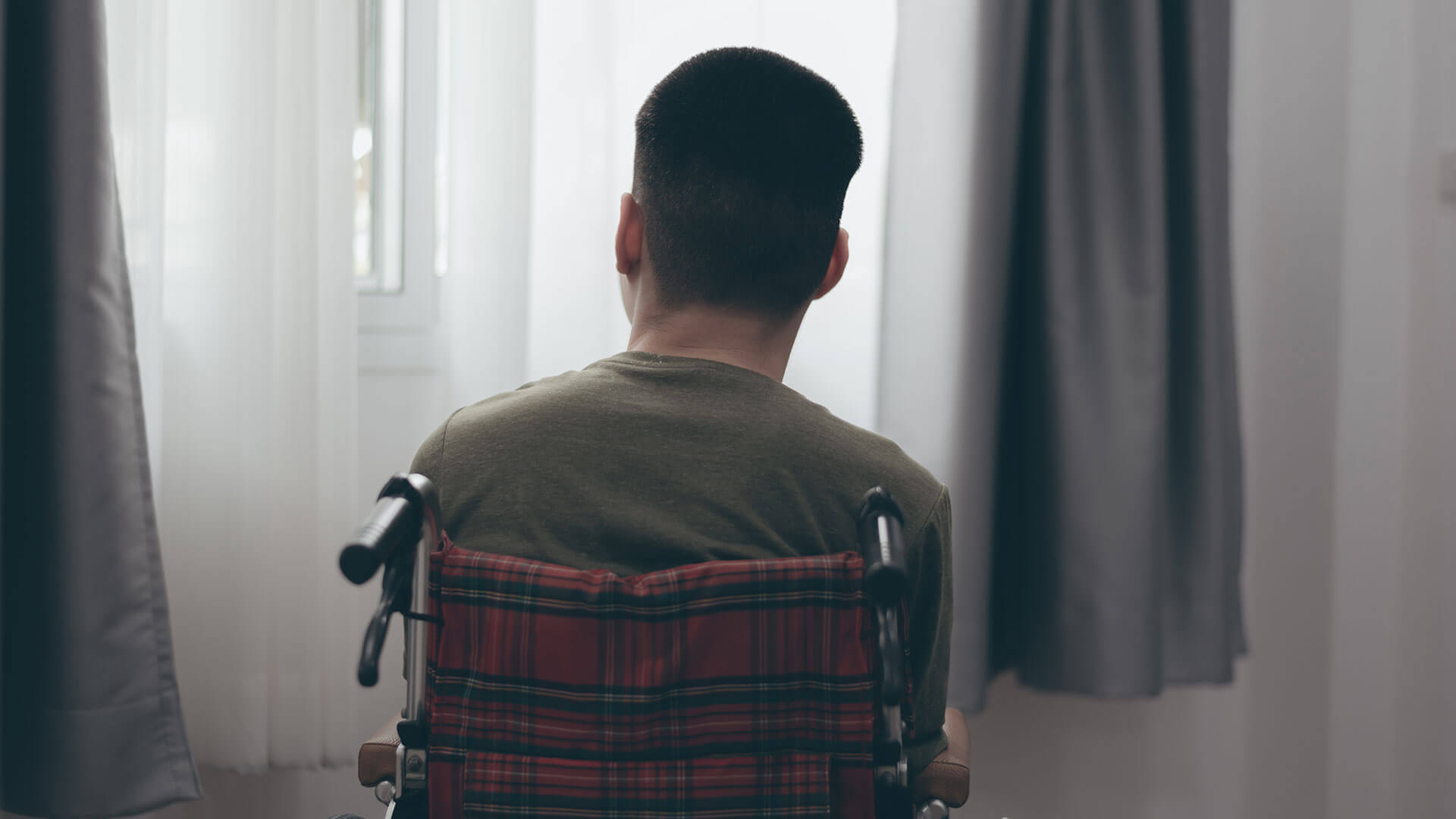 NDIS Review Underway: A man sits in a wheelchair looking out the window.